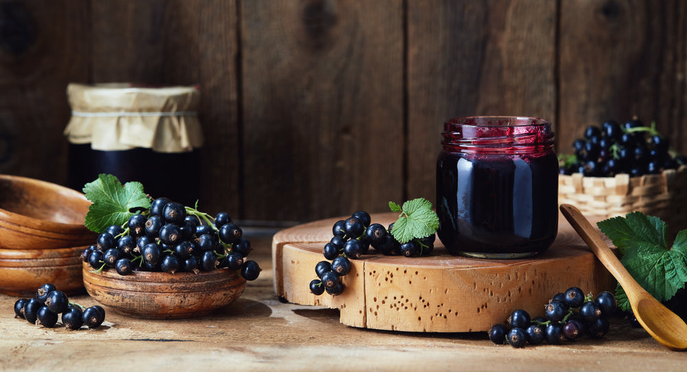 Photo of a rusitc table with wood bowls and stands.  Black Currants littered on top with a jar of black currant jam.